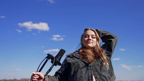 Young Woman Singing With Microphone Outdoors in Field