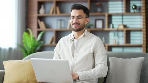 Man Relaxes on Couch Typing on Laptop at Home