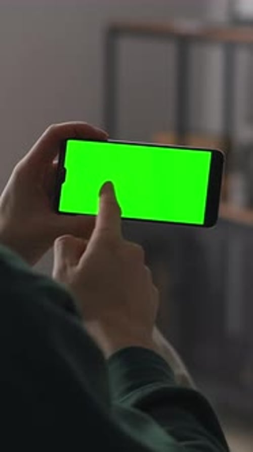 Person Holding and Interacting with a Smartphone Displaying a Vivid Green Chroma Key Screen
