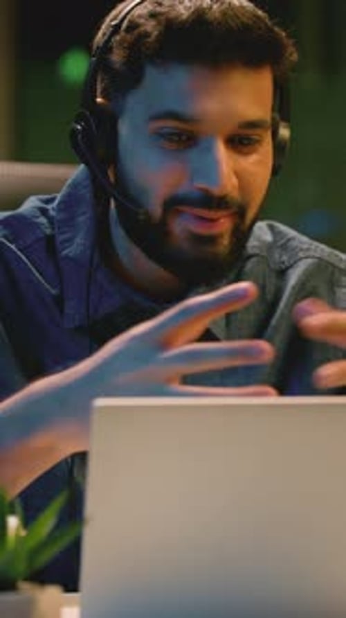 Carefree, heureux homme d'affaires indien, parlant avec un ordinateur portable, appel vidéo, portant un casque à la tombée de la nuit, au bureau