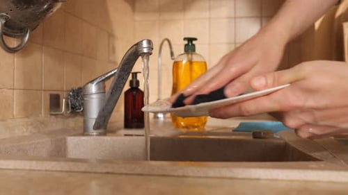 Hands Washing a Ceramic Plate Under a Running Kitchen Tap Soap Suds and Water Stream Visible As Part