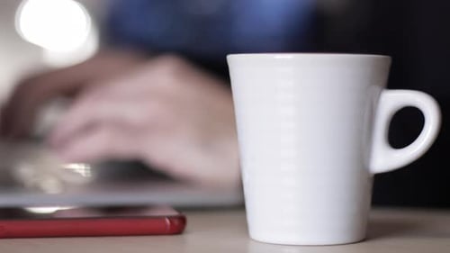 Man works on laptop in the office having a cup of tea. Closeup and slow motion