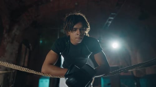 Focused Young Man Leans on Boxing Ring Ropes