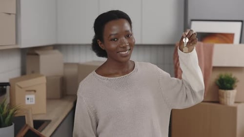 African American Woman Holding House Key Looking at Camera and Smiling Indoors in New Home
