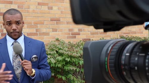 Man Speaking Into Microphone in Front of Brick Wall