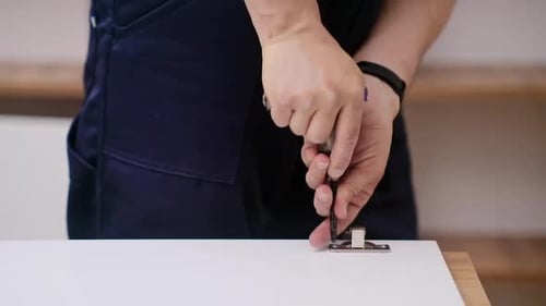 Man installs hinge on white cabinet with screwdriver