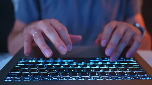 Nahaufnahme von Finger, die nachts Code eingeben, in den blaublauen Farben der Hintergrundbeleuchtung der Laptop-Tastatur