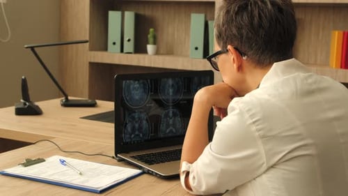 Doctor Analyzing Brain Scans on Laptop in Office