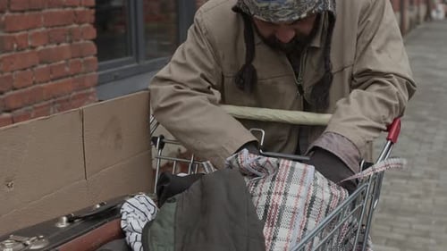 Man Searching Shopping Cart Contents in Urban Environment