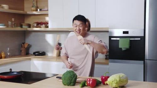 Couple dancing and singing in kitchen with vegetables