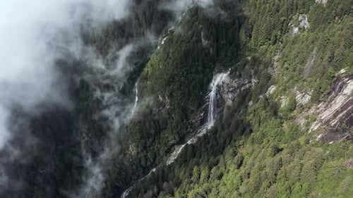 drone aerial view of a waterfall and a torrent on the side of a mountain, big cloud hiding the fores