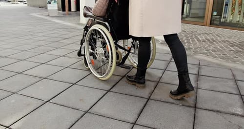 Woman Pushing Wheelchair on City Sidewalk