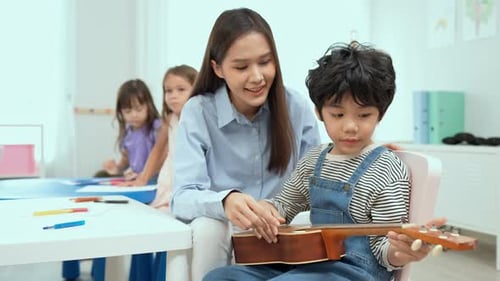 Teacher Helps Young Boy Play Guitar in Classroom