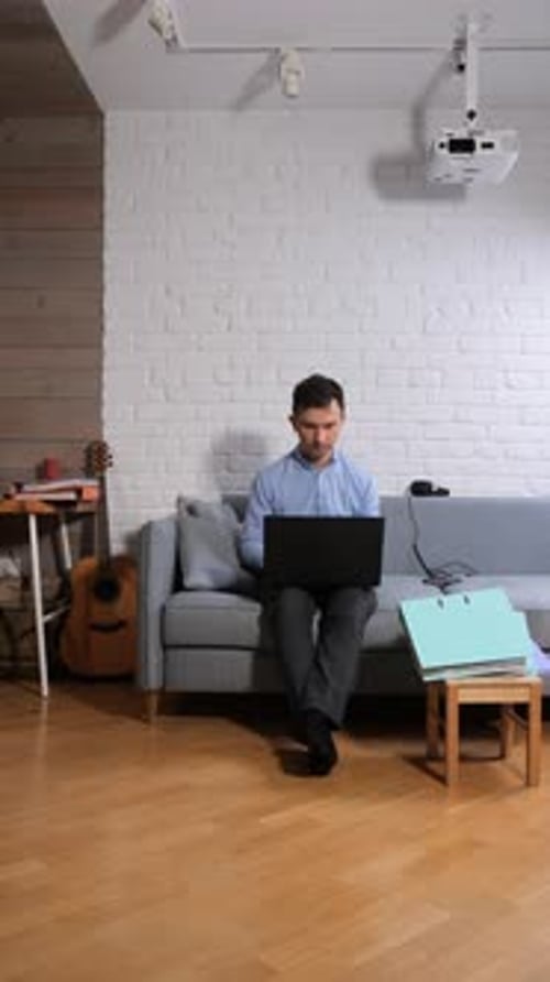 Man Works on Laptop Sitting on Couch at Home