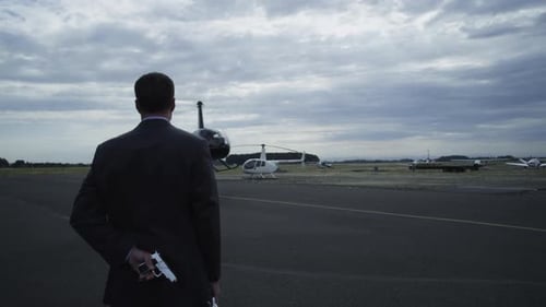 Un hélicoptère atterrit devant un homme d'affaires dissimulant une arme dans le dos