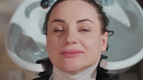 Woman Sitting at Salon Wash Station with Fresh Rinsed Hair Smiling Softly and Enjoying Warm Scalp