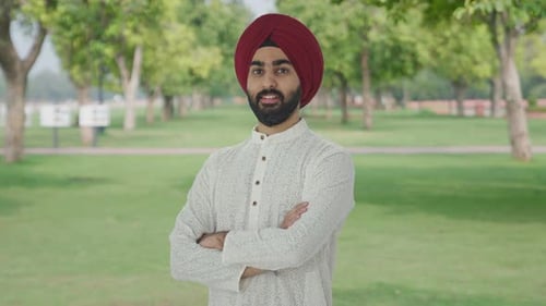 Portrait of Happy Sikh Indian man standing crossed hands in park