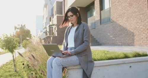 Woman typing text on laptop sitting on street during break time working. Outdoors