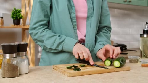 Woman Cutting Cucumber on Board in Kitchen