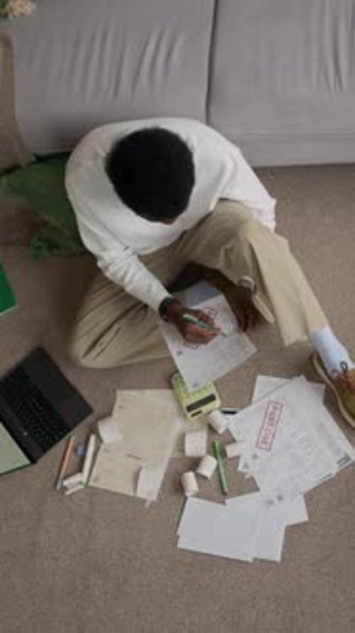 Vertical of Concerned Man Managing Household Expenses on Living Room Floor