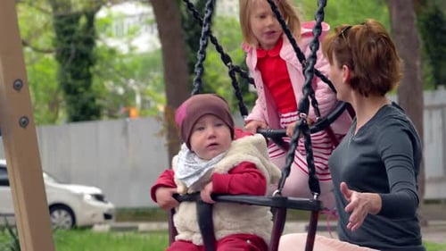 Spielplatz, Kinder - Mama auf dem Spielplatz schiebt ihre Kinder auf die Schaukel