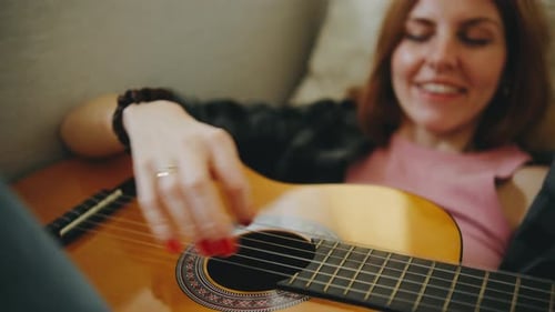 Woman playing guitar while relaxing on couch