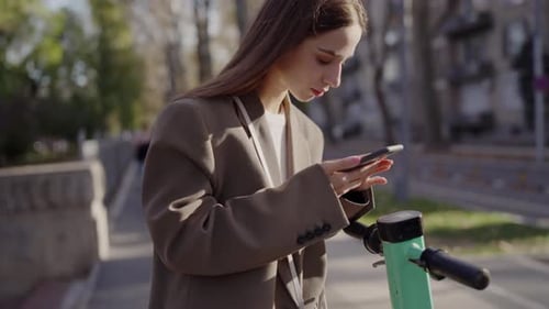 Young Woman Using Smartphone Near Electric Scooter in City