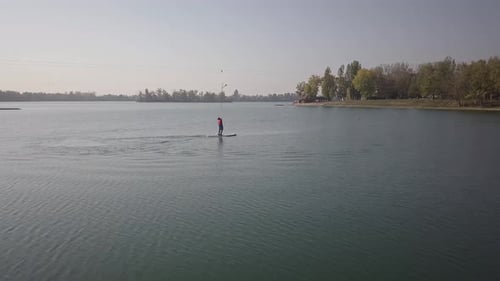 Drone shot of a person paddle boarding on a lake on a sunny day