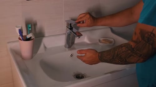Hombre milenario caucásico tatuado que hace higiene matutina se lava las manos con agua limpia del grifo