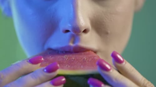 Close Up Of Woman's Mouth Taking a Bite and Eating Watermelon Fruit, Studio Shot With Colorful Light