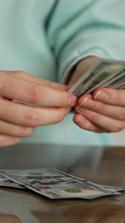 Woman counting hundred dollar bills on a table