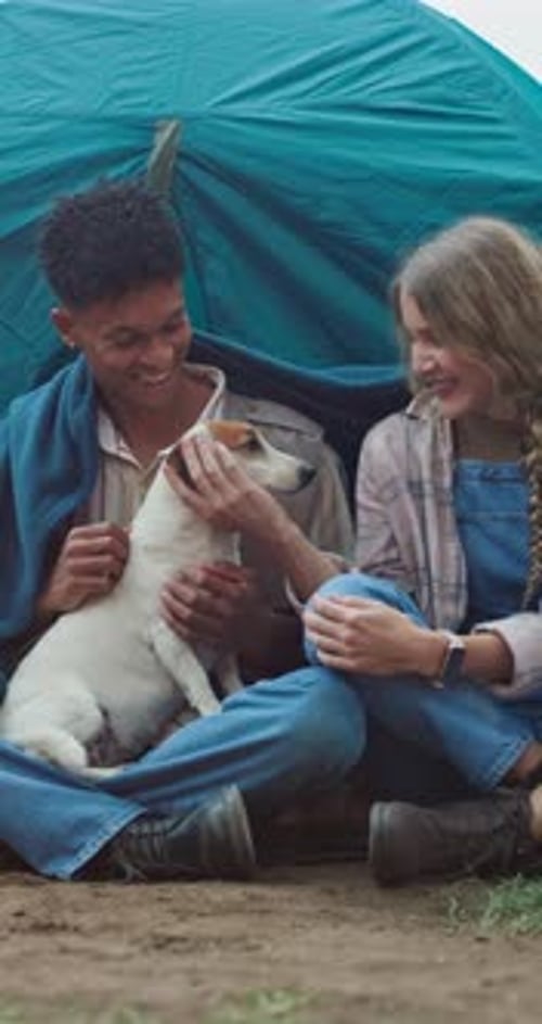 Young friends camping cuddling dog inside tent