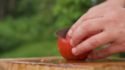 Male hands cutting tomato in halves on wooden board, close shot