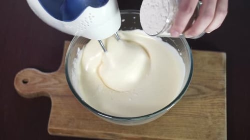 Cook adds flour to glass bowl mixing dough with motor mixer for sweet food
