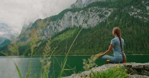 Woman meditating by the serene Gosau lake, framed by green grass and distant peaks