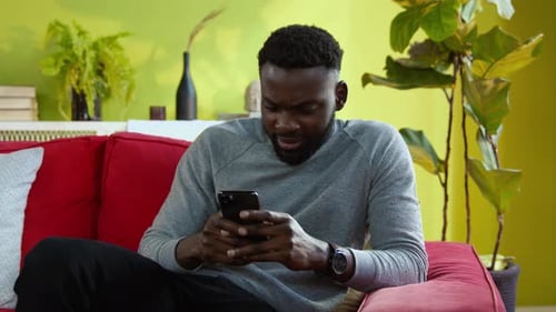 Man Sitting on Couch Using Smartphone at Home