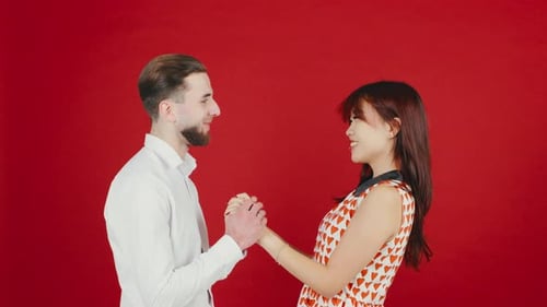 Young Adult Couple Holds Hands Against Red Backdrop