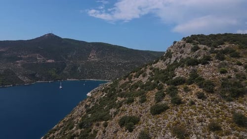 Sailing Yacht Sits in a Beautiful Bay Drone Flies Out From Behind a Mountain