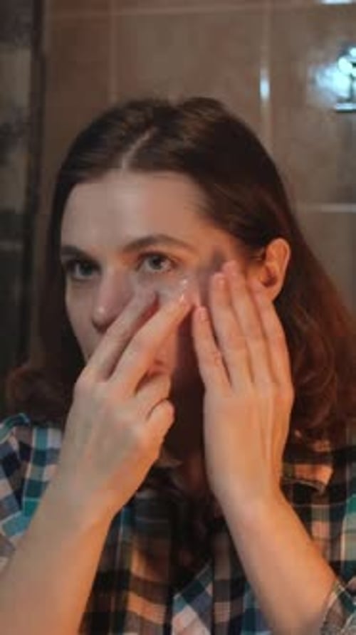 Vertical Video Woman Applying Eye Patch Looking Into Bathroom Mirror
