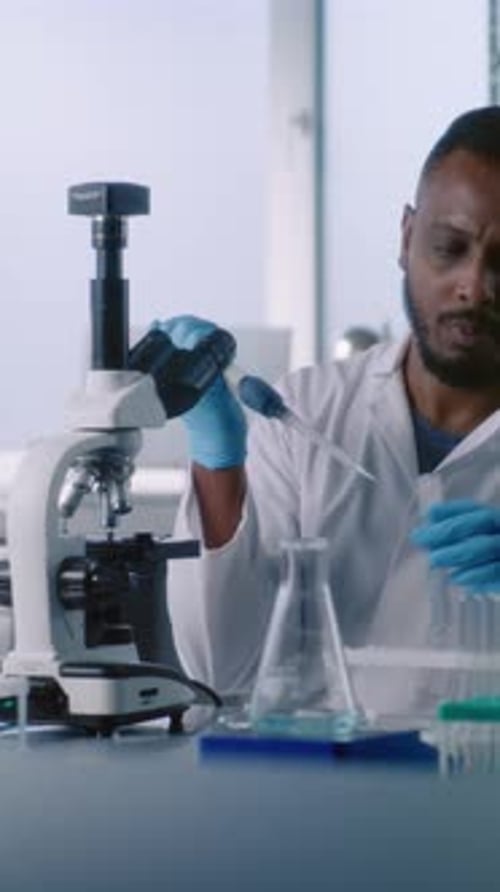 African American Microbiologist Takes Liquid From Test Tube Looks Under Microscope