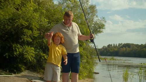 Glücklicher kleiner Junge und stolzer Vater halten Angelrute mit First Catch By River