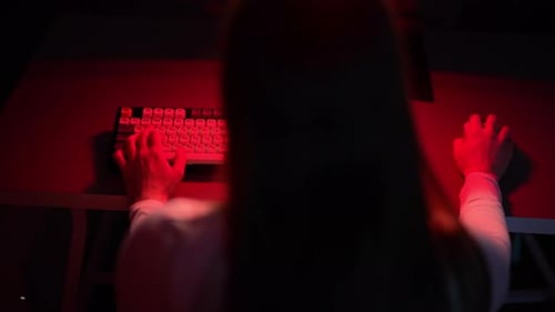 Rear View of Unrecognizable Female Gamer Using Wireless Computer Mouse and Typing on Neon Keyboard