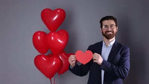 St. Valentine's Day. Man with paper heart and balloons on grey background