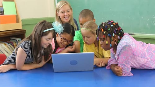 Teacher and students collaborate on a laptop in a school classroom environment