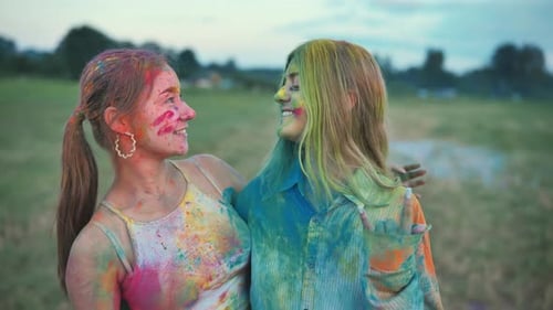 Two Girls Covered with Colorful Holi Powder are Laughing and Enjoying the Event on a Field