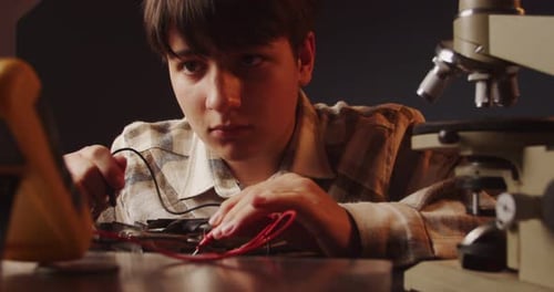Adolescente concentrado que trabaja con un multímetro y observa las lecturas en el monitor: algo fascinante
