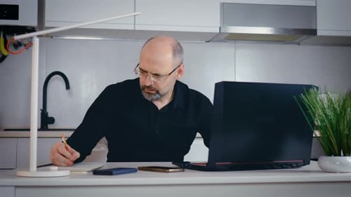 Man Working at Laptop Taking Notes at Home