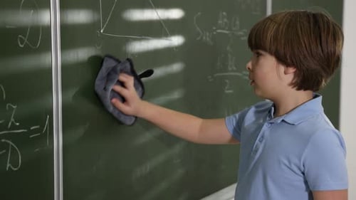 Boy Cleans Chalkboard in Classroom with Eraser