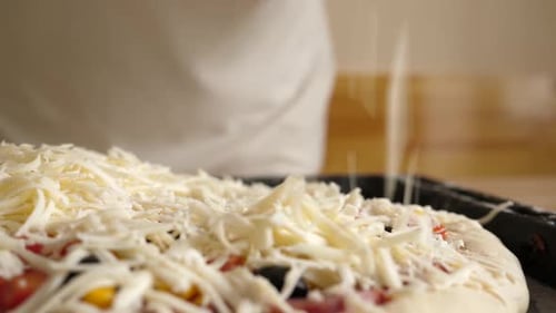 41. A woman adds cheese while cooking a pizza. Cooking pizza at home.