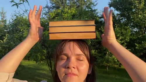 Woman Balancing Books on Head with Closed Eyes Outdoors at Sunset